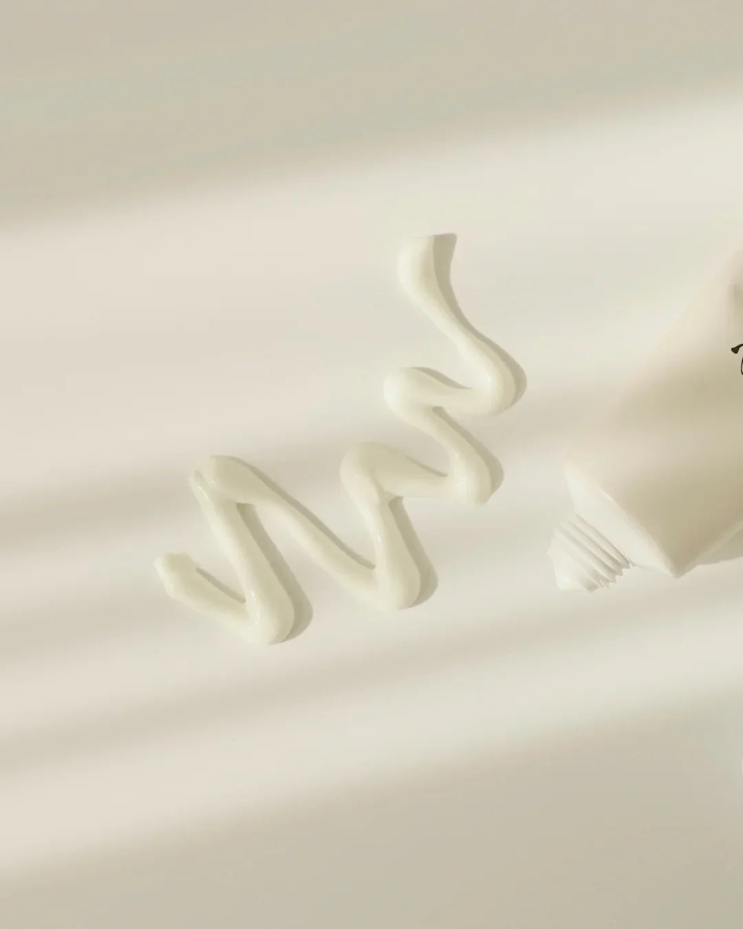 Creamy white texture of sunscreen or skincare cream squeezed from an off-white tube on light background