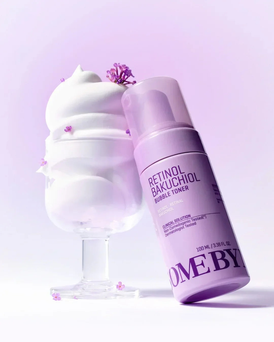 Retinol Bakuchiol Bubble Toner bottle next to whipped white foam in glass with small purple flowers