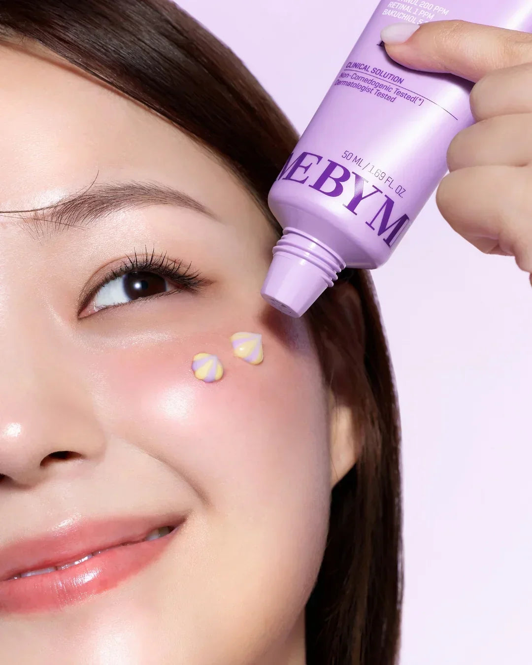 Close-up of woman applying dual cream with retinol and bakuchiol in purple tube to cheek