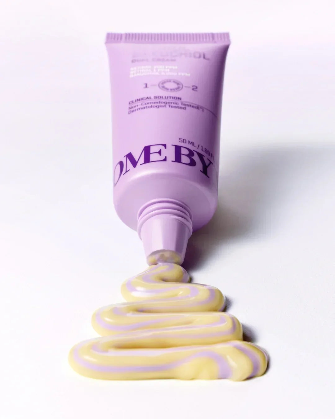 Lavender tube of retinol bakuchiol dual cream with swirled yellow and purple cream on white surface