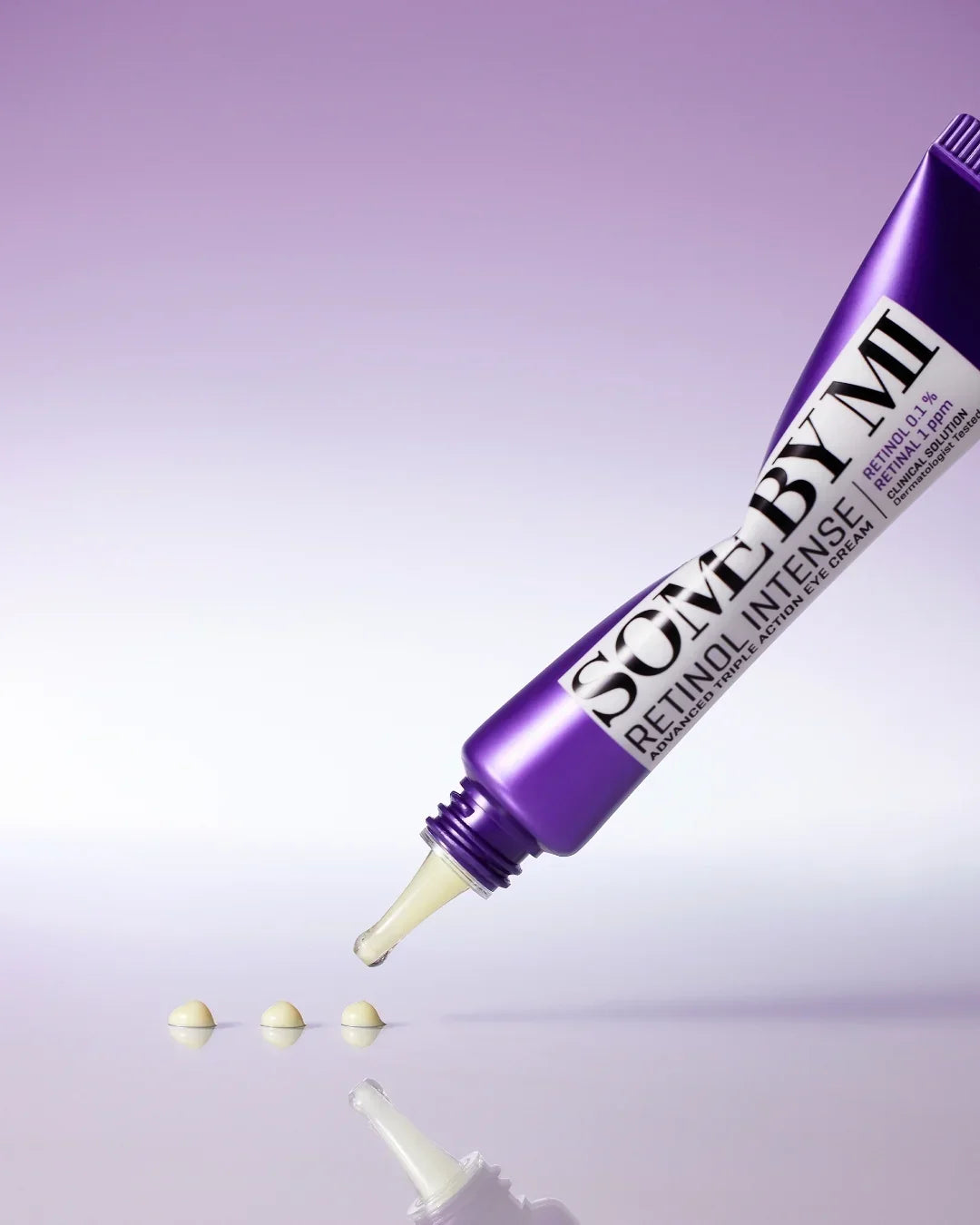 Close-up of purple SOMEBYMI Retinol Intense eye cream tube with drops on reflective surface and purple gradient background