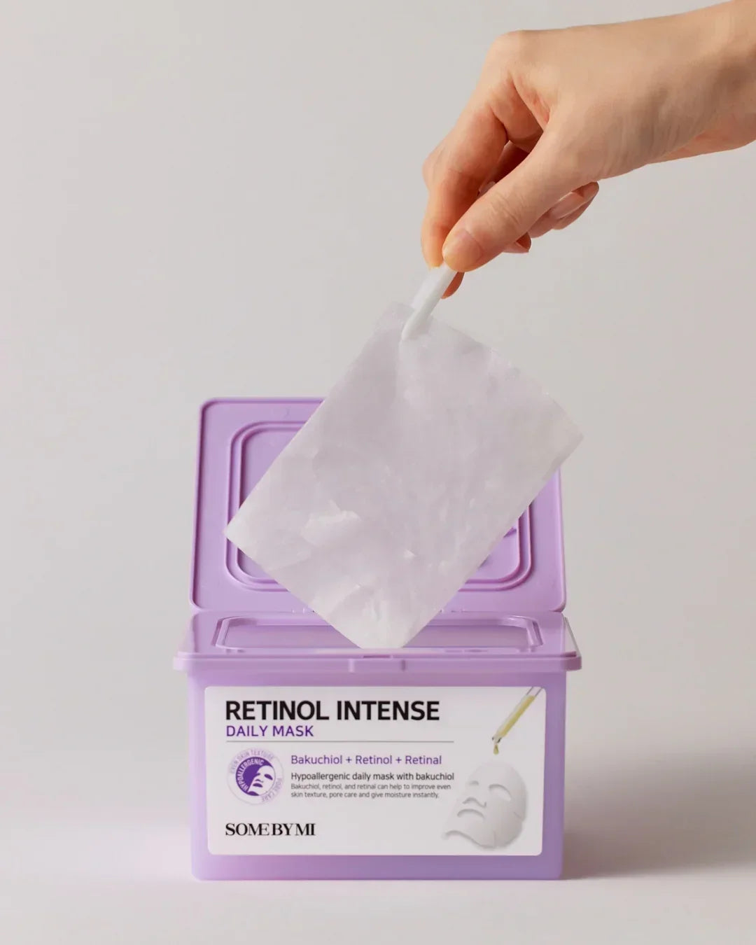 Hand removing a white retinol intense daily mask sheet from a purple SOME BY MI container