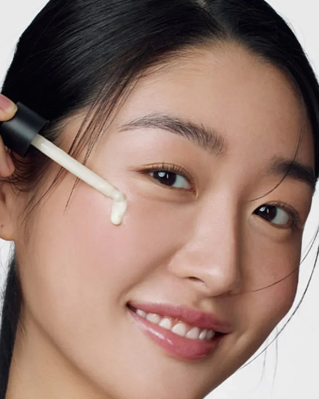 Close-up of woman applying retinol serum with dropper on cheek, clear skin, skincare beauty