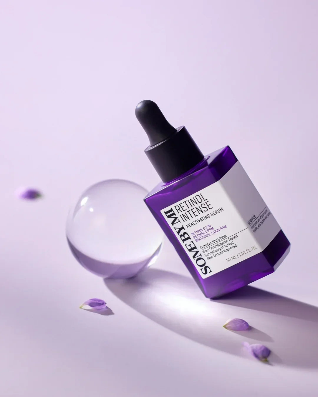 Purple bottle of Some By Mi Retinol Intense Reactivating Serum with dropper on lavender background with clear glass orb and small violet petals
