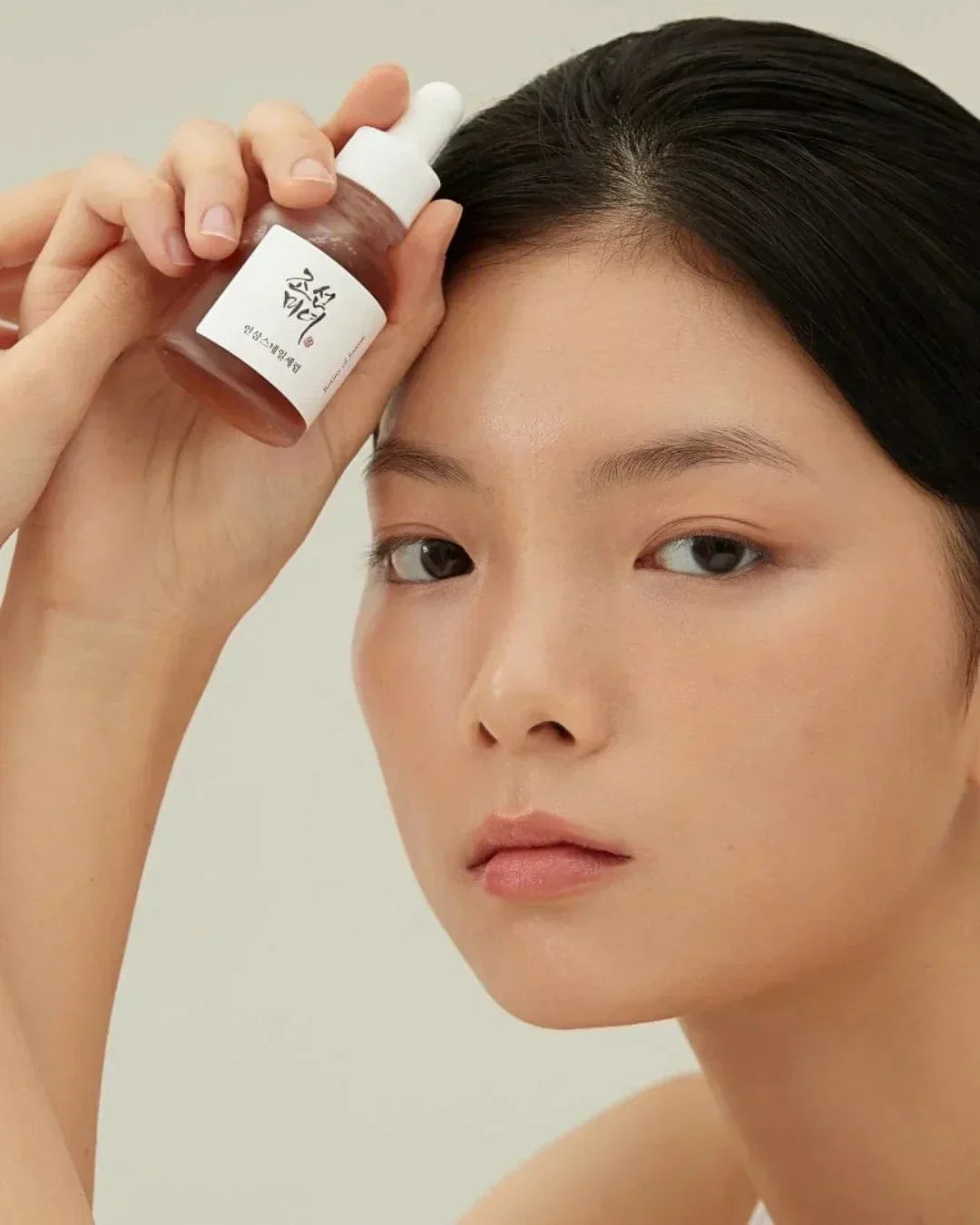 Close-up of woman holding ginseng snail mucin serum bottle near her face with clear skin