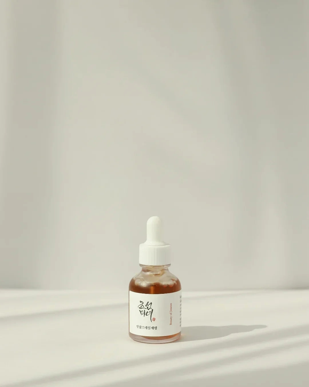 Small amber dropper bottle of Asian skincare serum on white surface with soft shadows