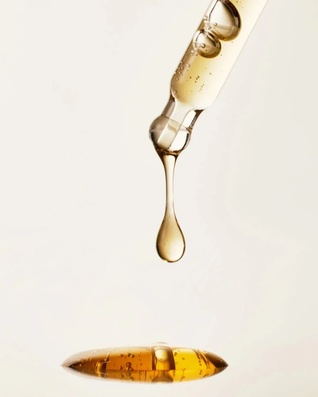 Close-up of golden serum drop falling from a glass dropper onto a liquid surface