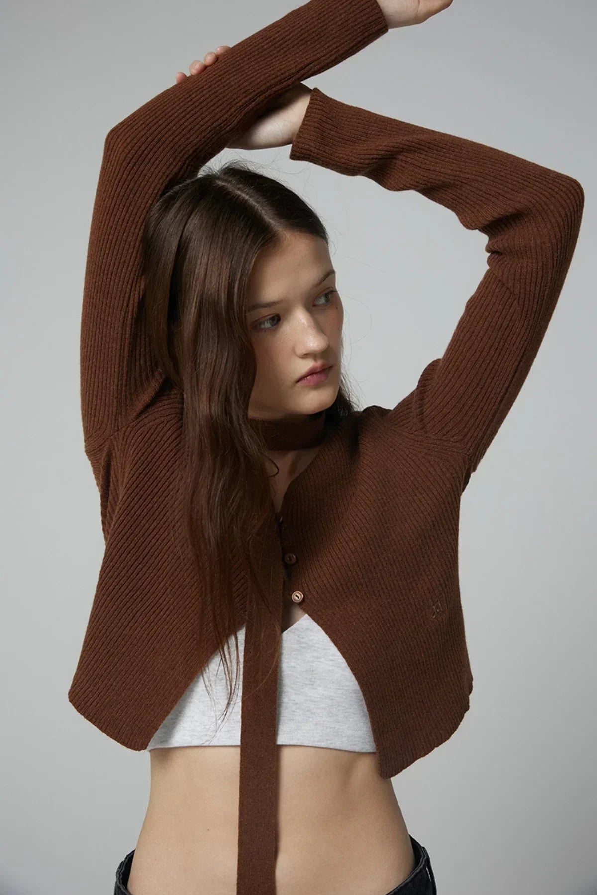 Close-up of a woman wearing a brown ribbed V-neck open cardigan with long sleeves over a light gray crop top