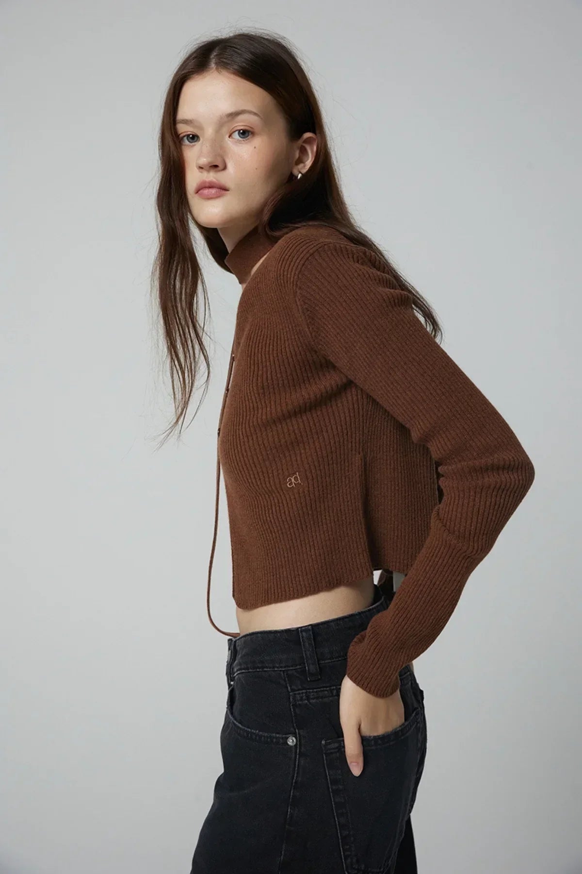 Side view of woman wearing brown ribbed cropped cardigan and black jeans on gray background