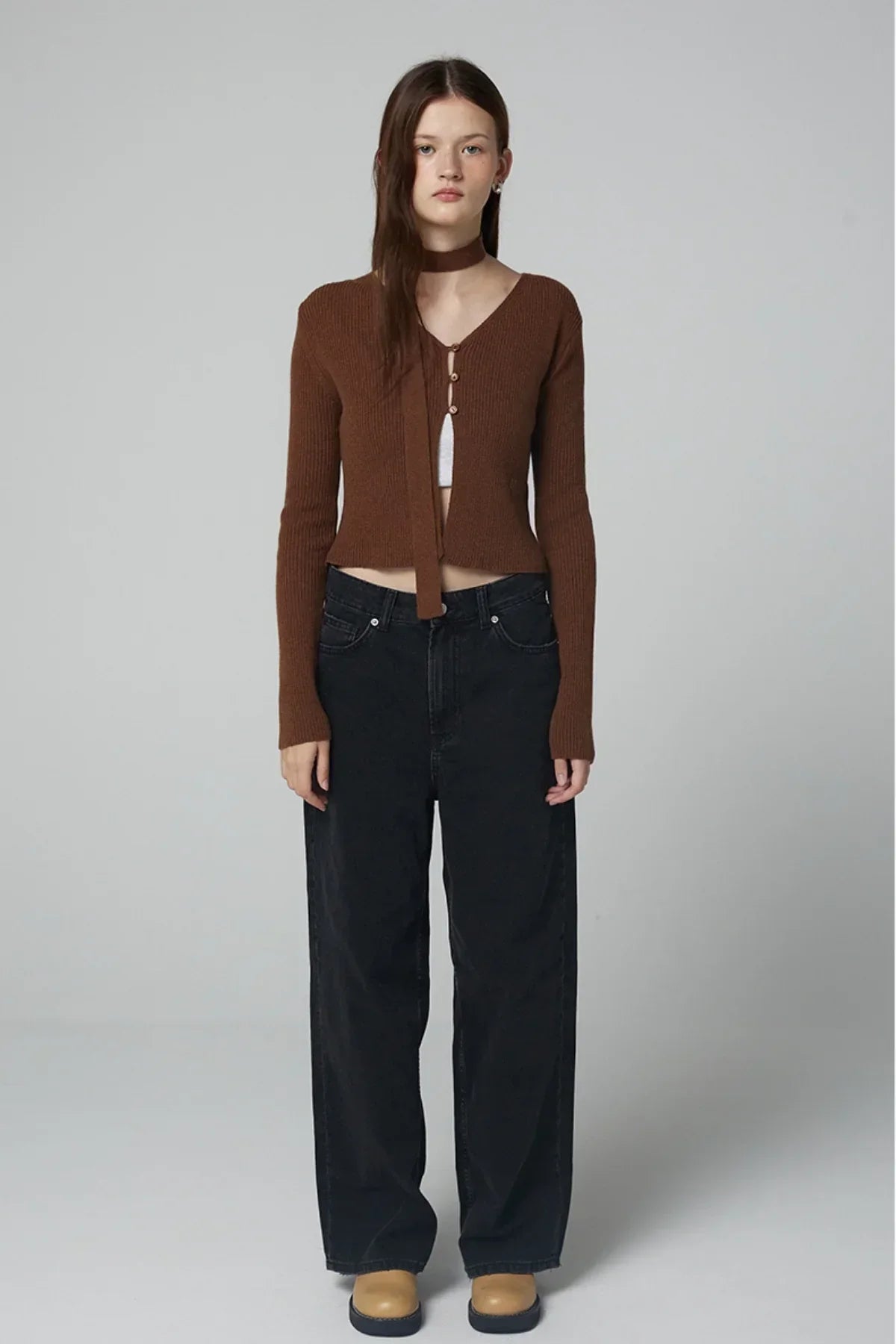 Woman wearing ribbed brown V-neck cardigan with buttons, black wide-leg jeans, and tan shoes