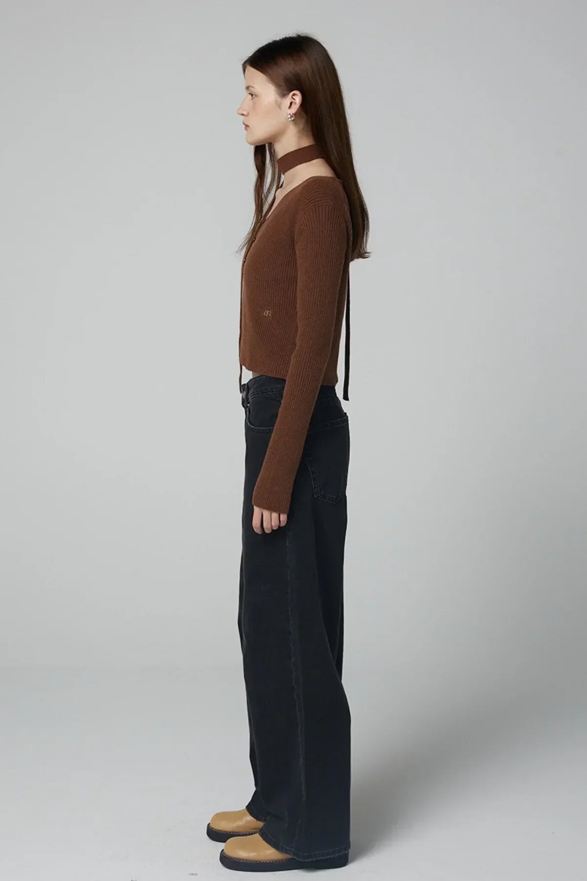 Side view of woman wearing brown ribbed V-neck cardigan with choker and black wide-leg jeans