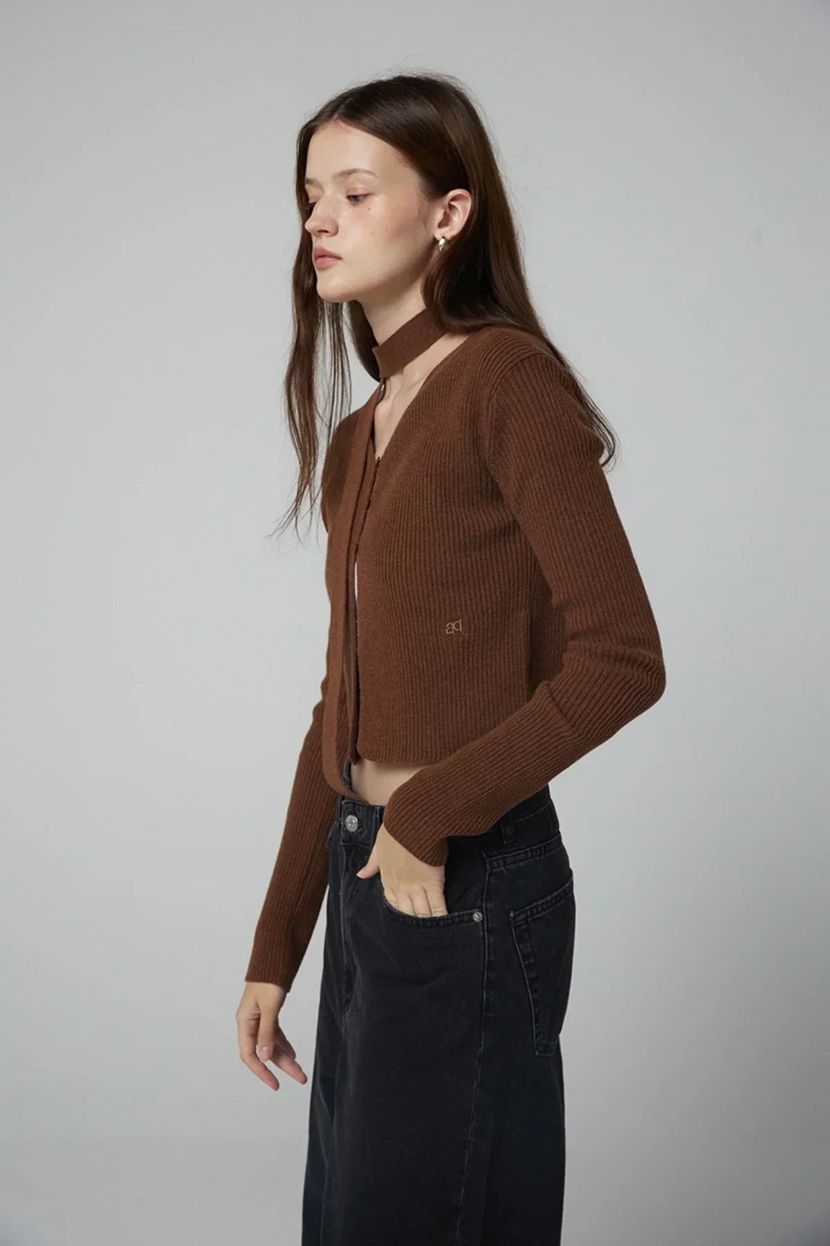 Woman wearing ribbed brown V-neck open cardigan with choker and high-waisted black jeans in studio