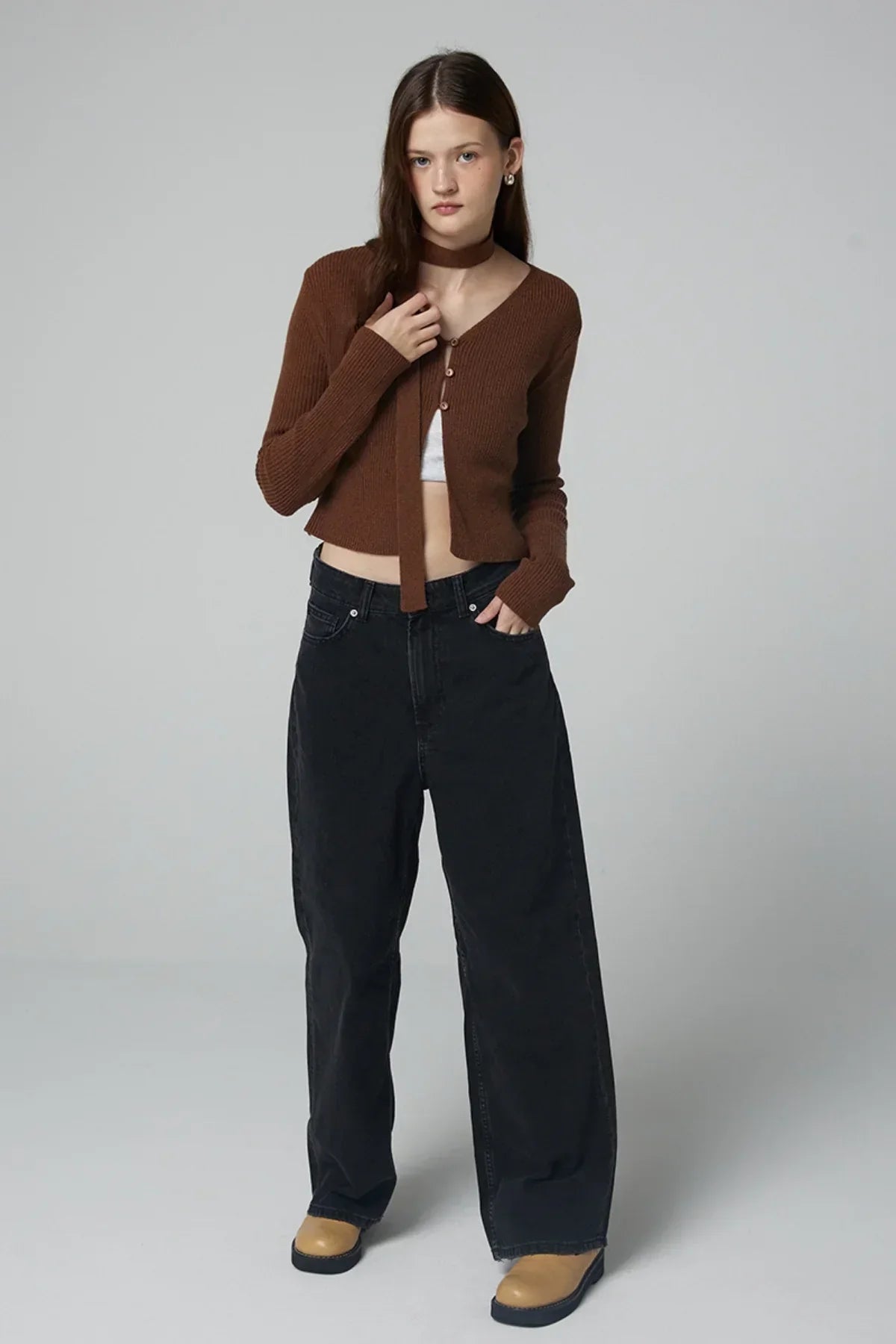 Woman wearing brown ribbed V-neck cardigan, black wide-leg jeans, and tan boots in studio