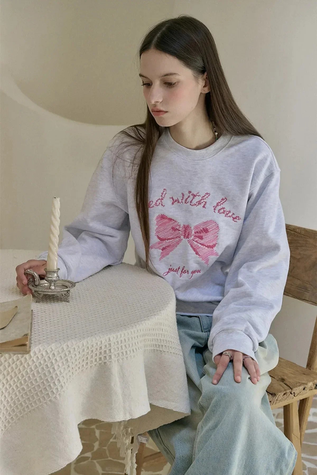 Young woman wearing grey sweatshirt with pink ribbon embroidery sitting at a table with white candle