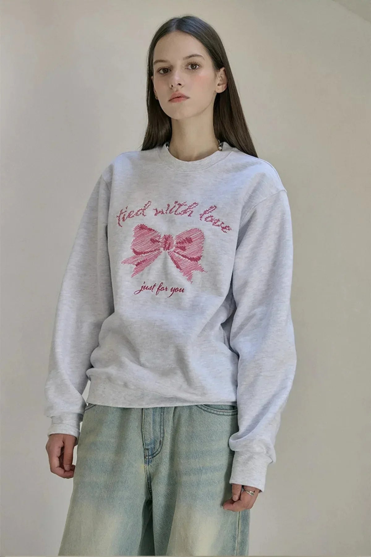 woman wearing grey sweatshirt with pink embroidered ribbon and text tied with love just for you