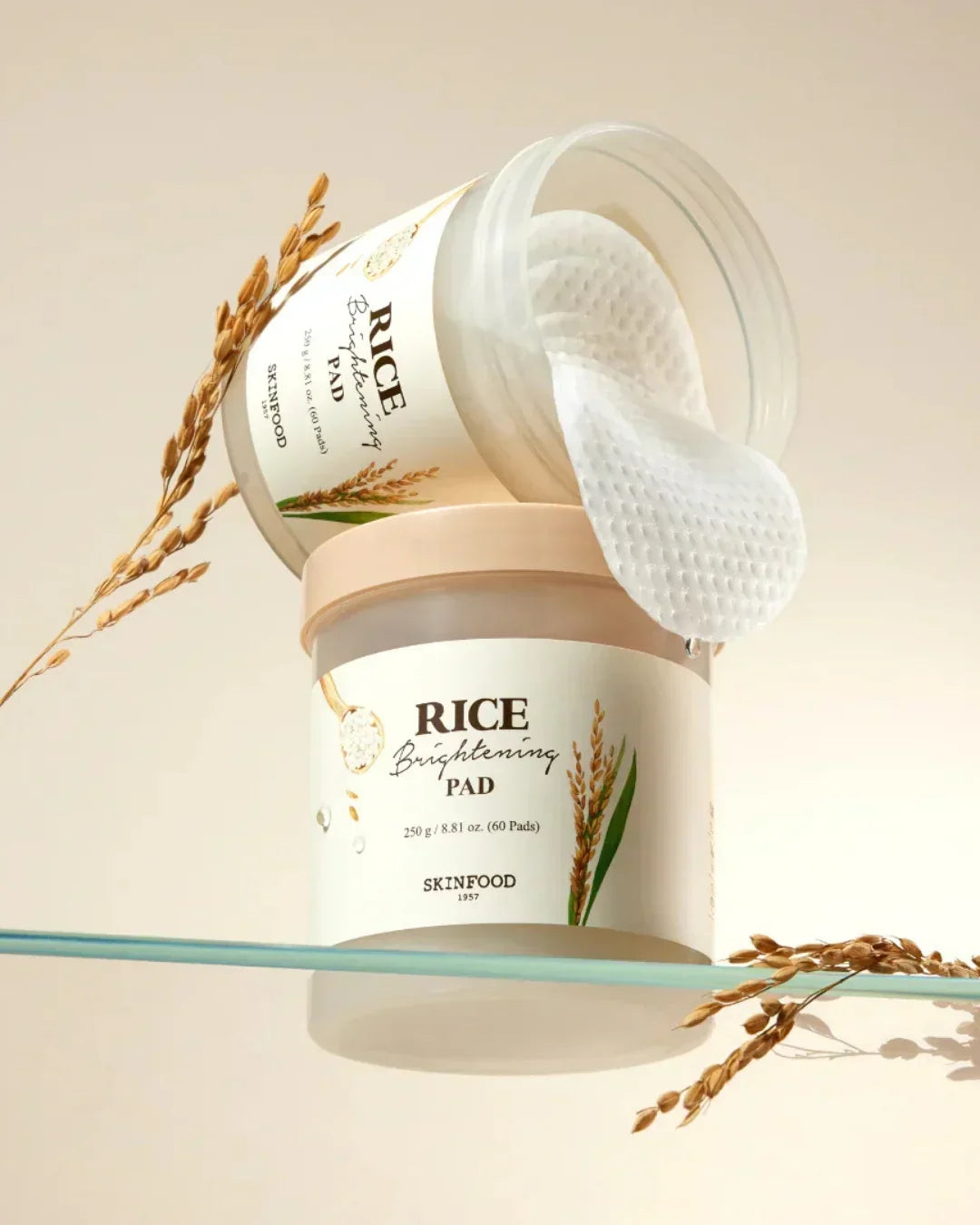 Skinfood Rice Brightening Pad container with round cotton pads and rice grains on a glass surface