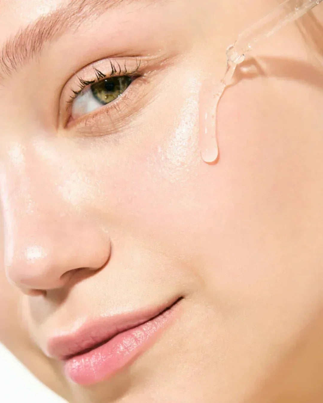 Close-up of woman applying clear hydrating serum with dropper on smooth skin