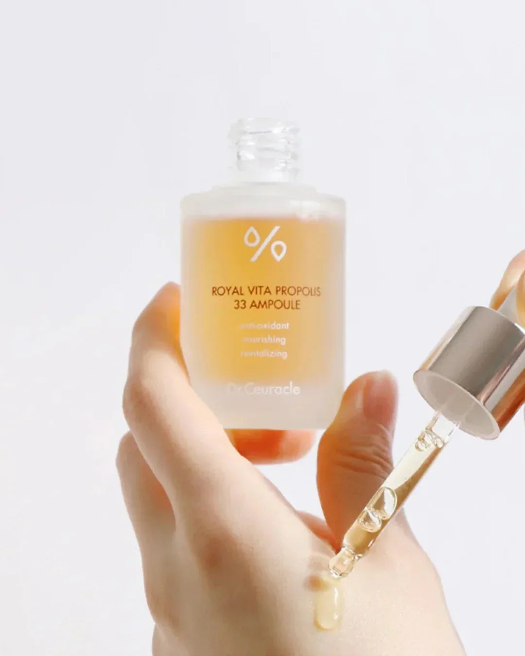 Hand holding Dr. Ceuracle Royal Vita Propolis 33 Ampoule with dropper applying serum on skin