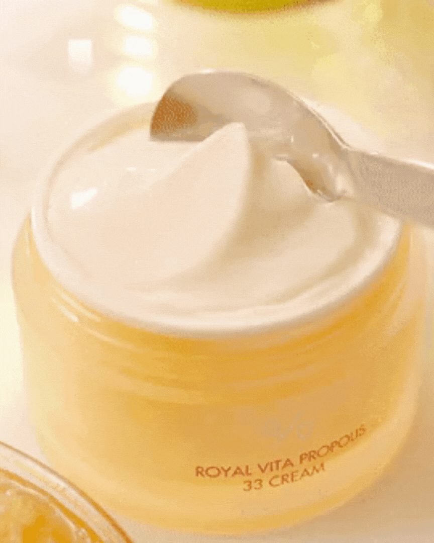 Yellow jar of Royal Vita Propolis 33 Cream with spoon scooping smooth white cream texture