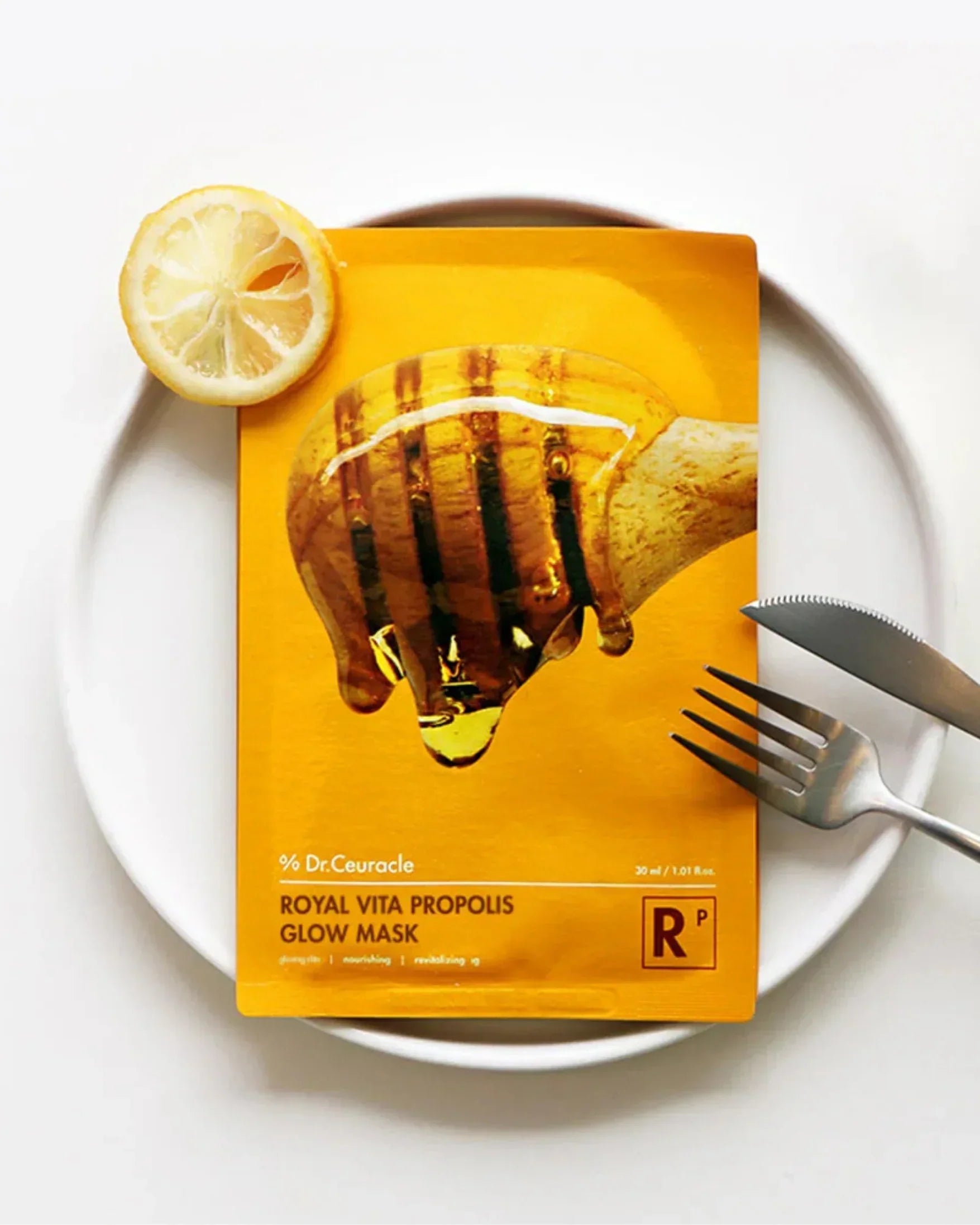 Royal Vita Propolis Glow Mask package on white plate with lemon slice, fork, and knife
