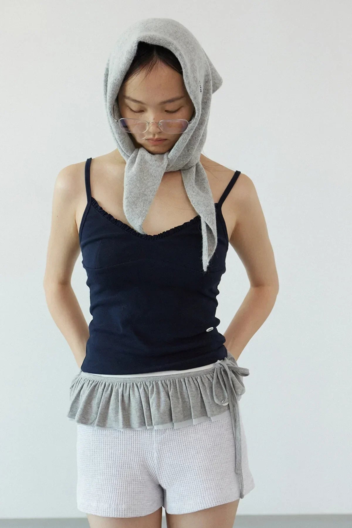Woman wearing navy ruffle bra top with grey tied scarf on head and white textured shorts