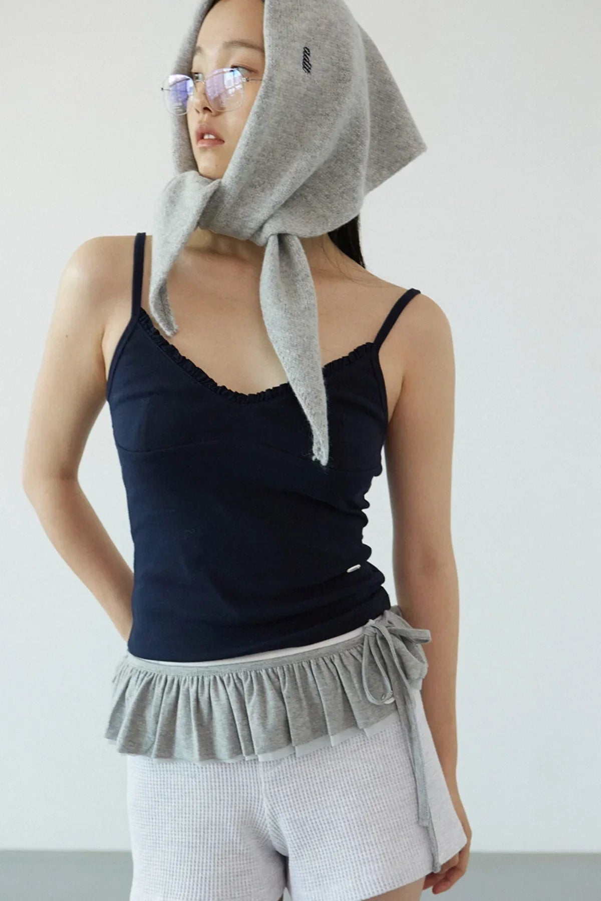 Close-up of a woman wearing a navy ruffle bra top with thin straps and a grey headscarf tied under the chin