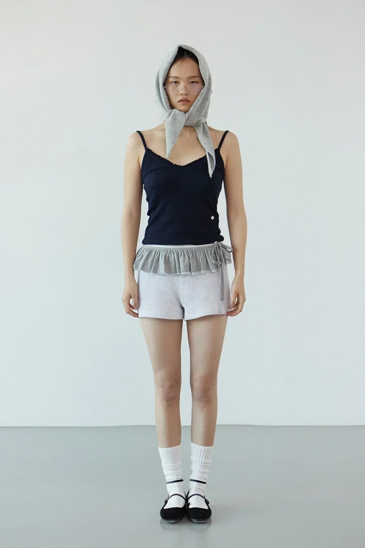 Model wearing navy ruffle bra top with gray ruffled shorts and matching headscarf in minimalist studio
