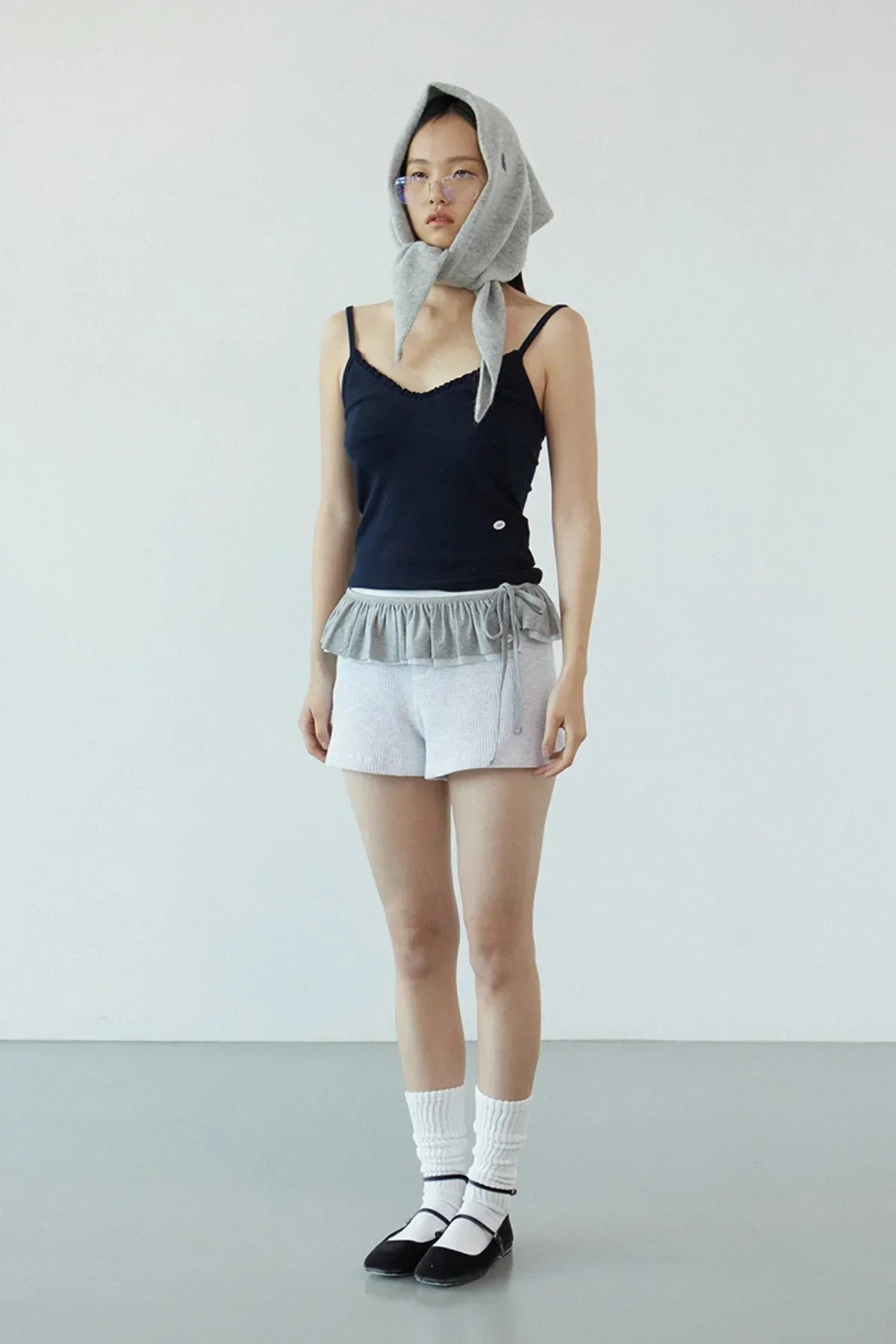 Model wearing navy ruffle bra top with light gray shorts, gray scarf hood, white socks, and black shoes