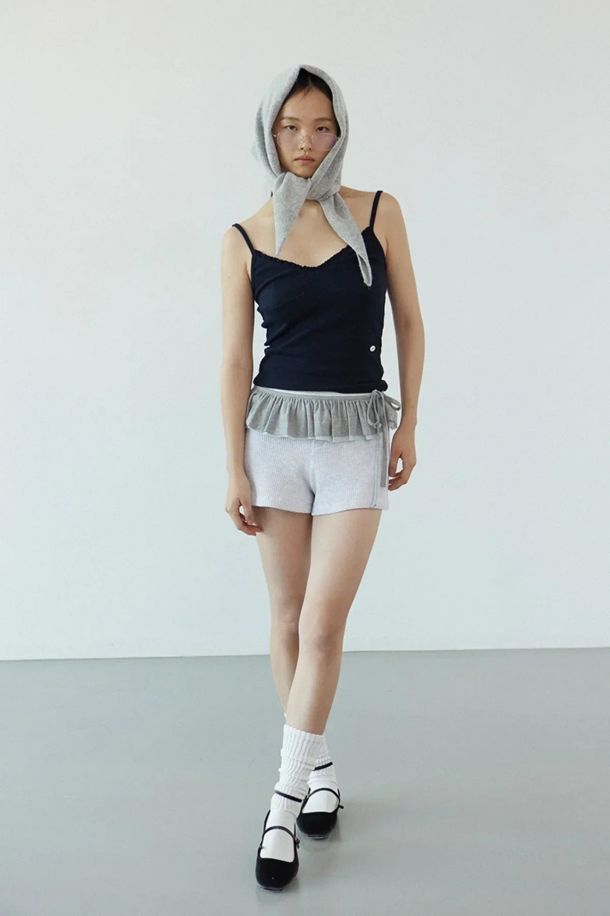 Model wearing navy ruffle bra top with gray shorts, white socks, black shoes, and gray headscarf in studio