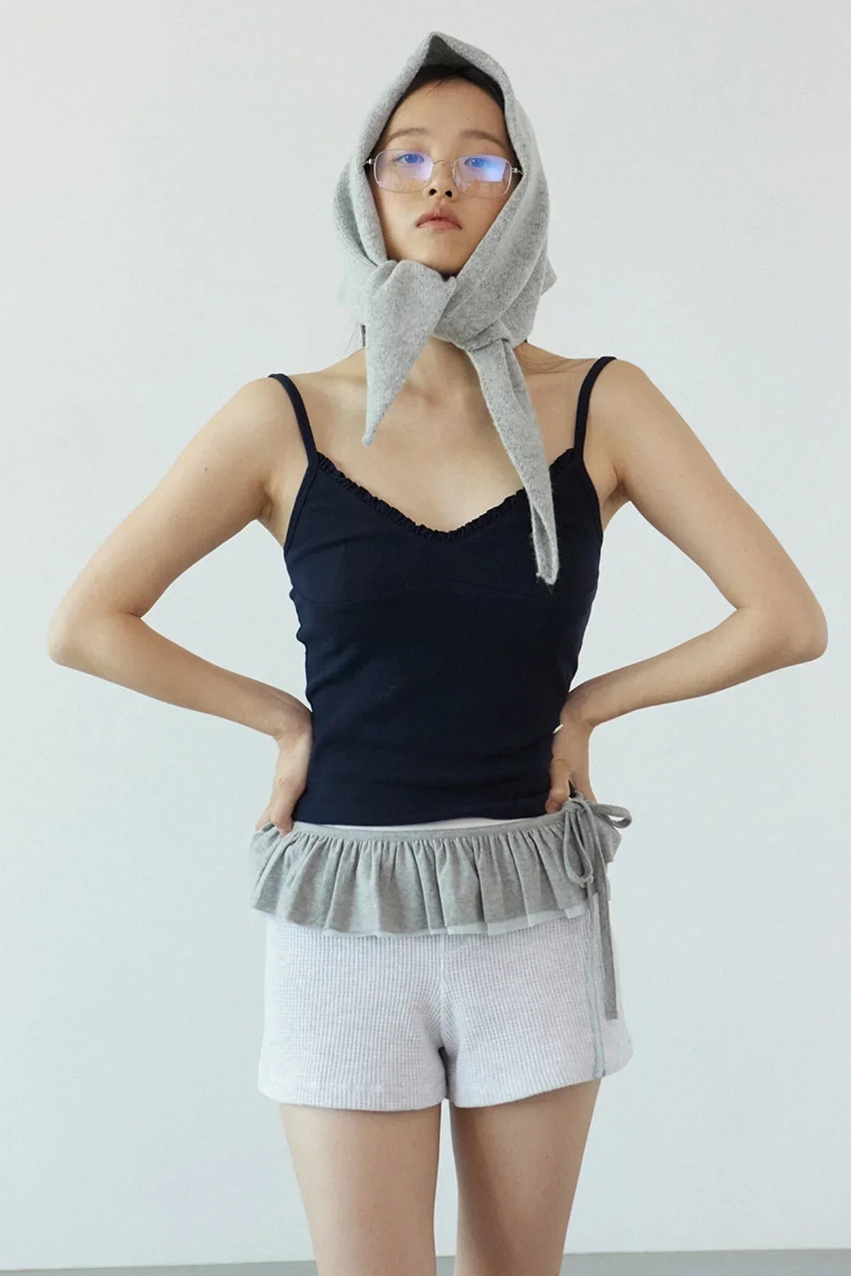 Woman wearing navy ruffle bra top and light gray shorts with a matching gray headscarf in minimalist studio
