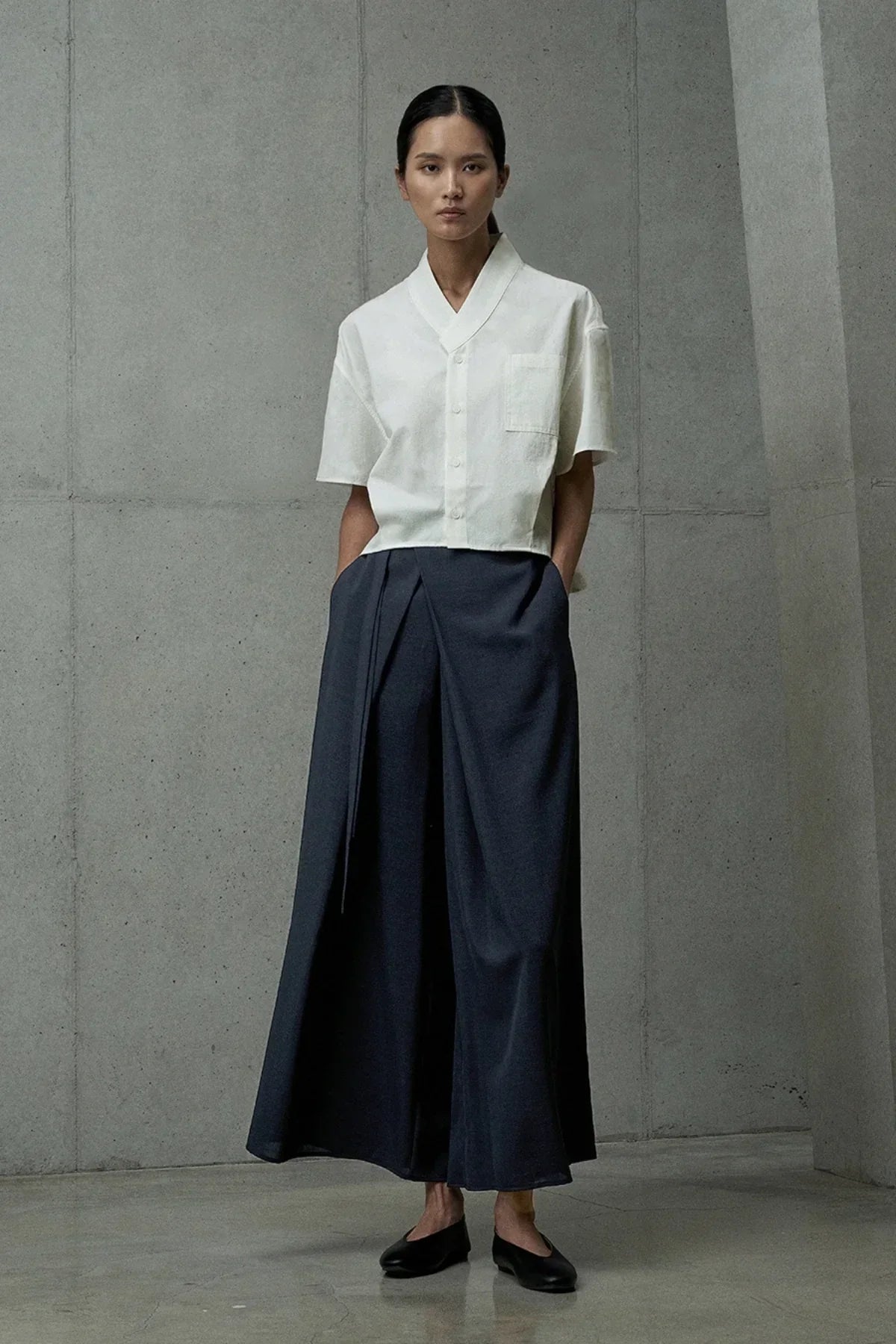 Woman wearing navy blue wide-leg pants with front pleat detail and white short-sleeve buttoned blouse