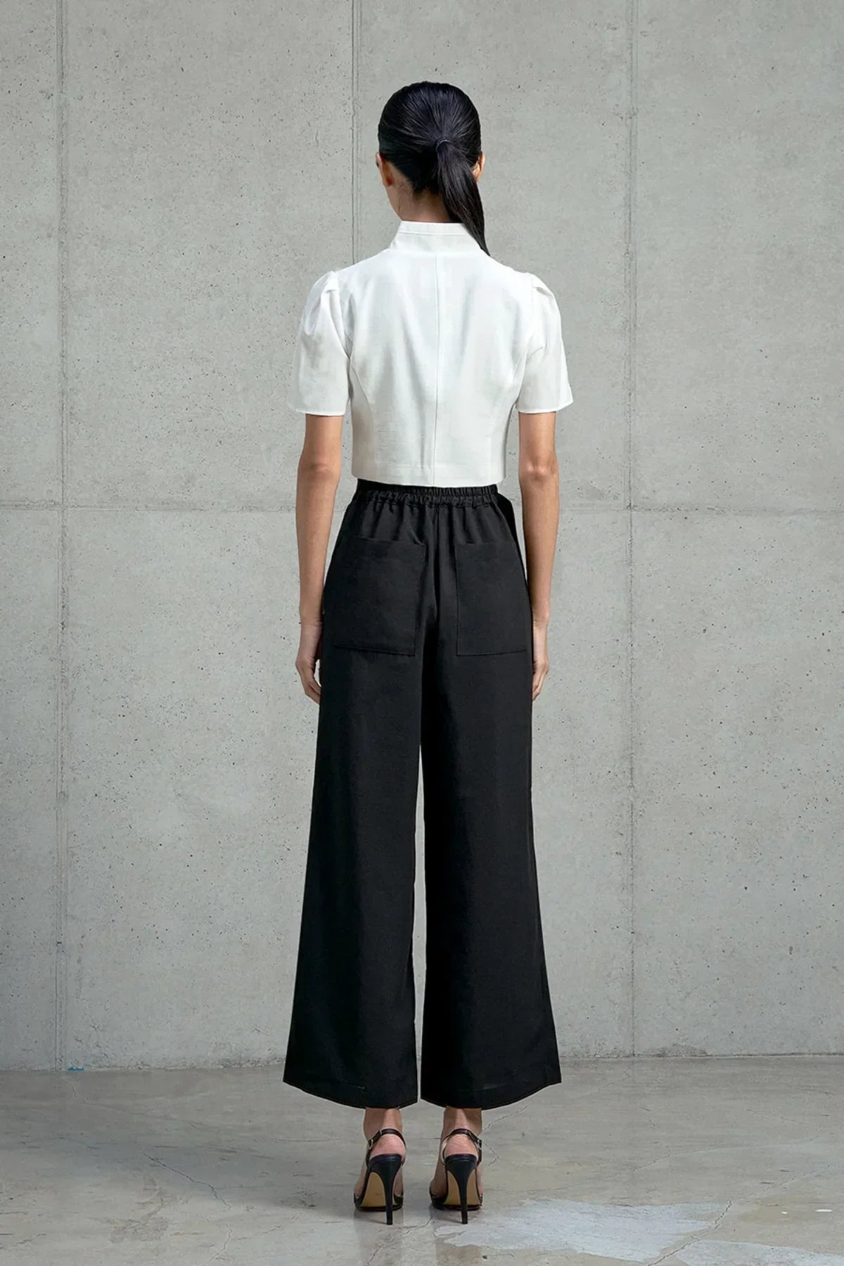 Woman wearing white short-sleeved jeogori top and black wide-leg pants with back pockets against a gray concrete wall