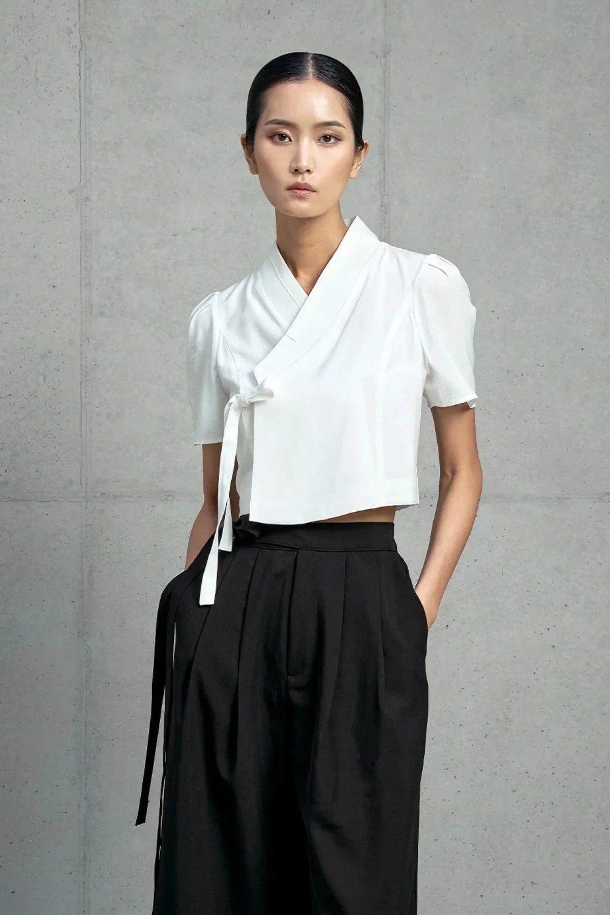 Model wearing white short-sleeved jeogori top and high-waisted black pants against gray concrete wall