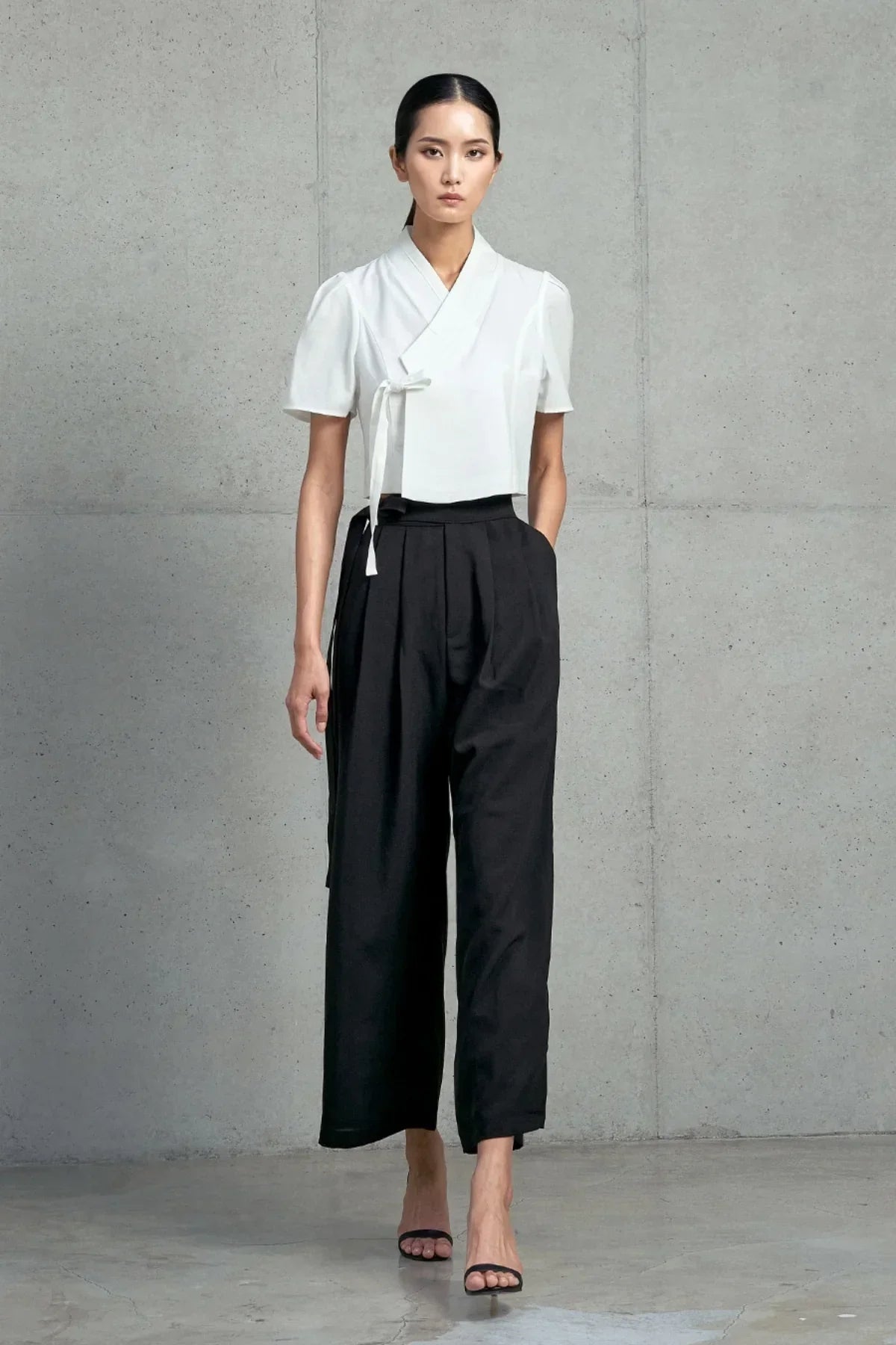Woman in modern Korean hanbok-inspired outfit with white short-sleeved jeogori and black high-waisted pants