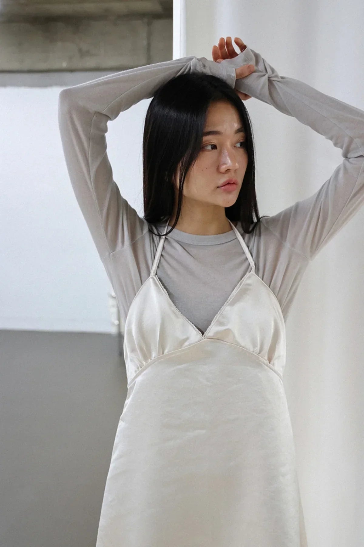 Woman wearing ivory satin bra mini dress over long sleeve gray top posing indoors