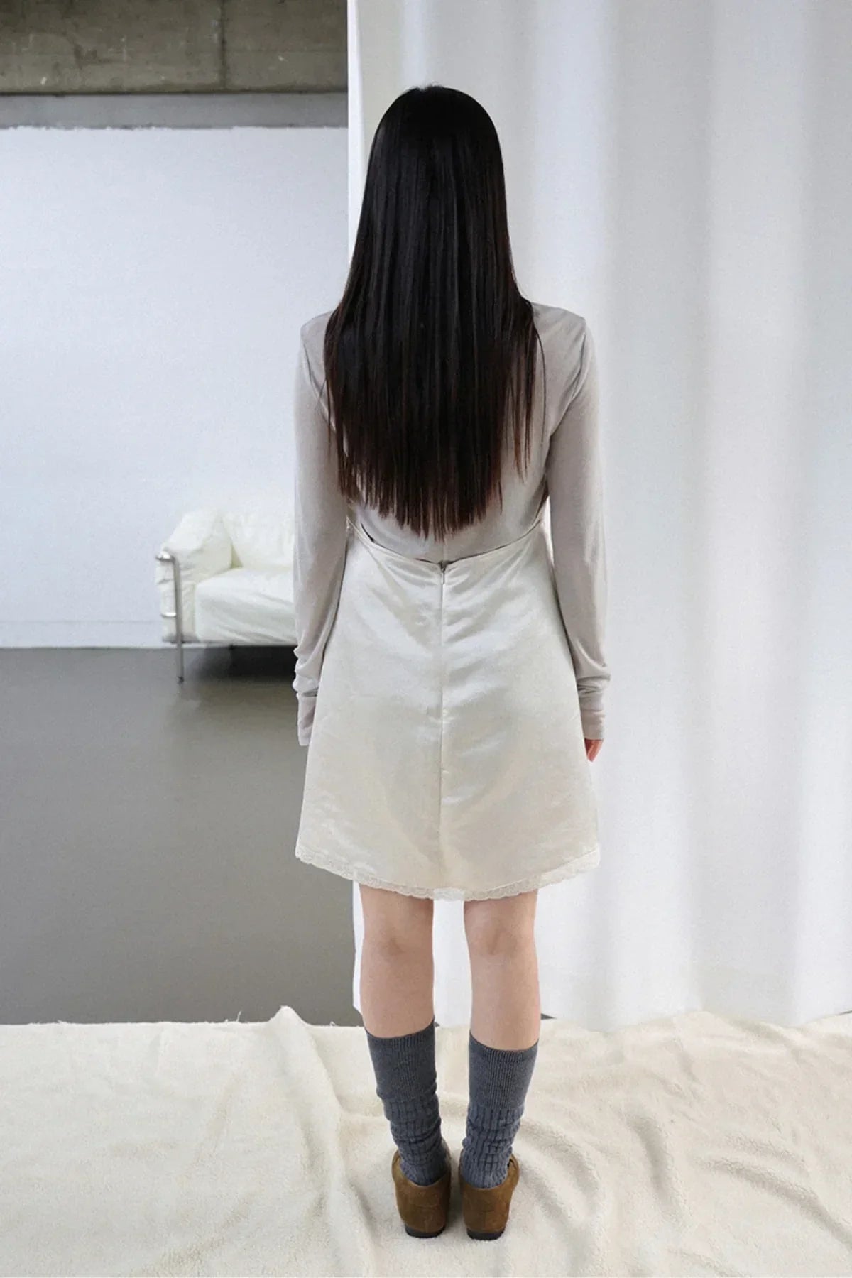 Woman wearing ivory satin mini dress and gray socks standing indoors with white sofa in background