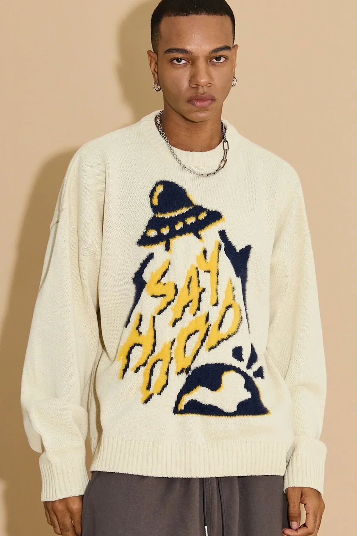 Young man wearing ivory knit sweater with UFO and SAY HOOD graphic design