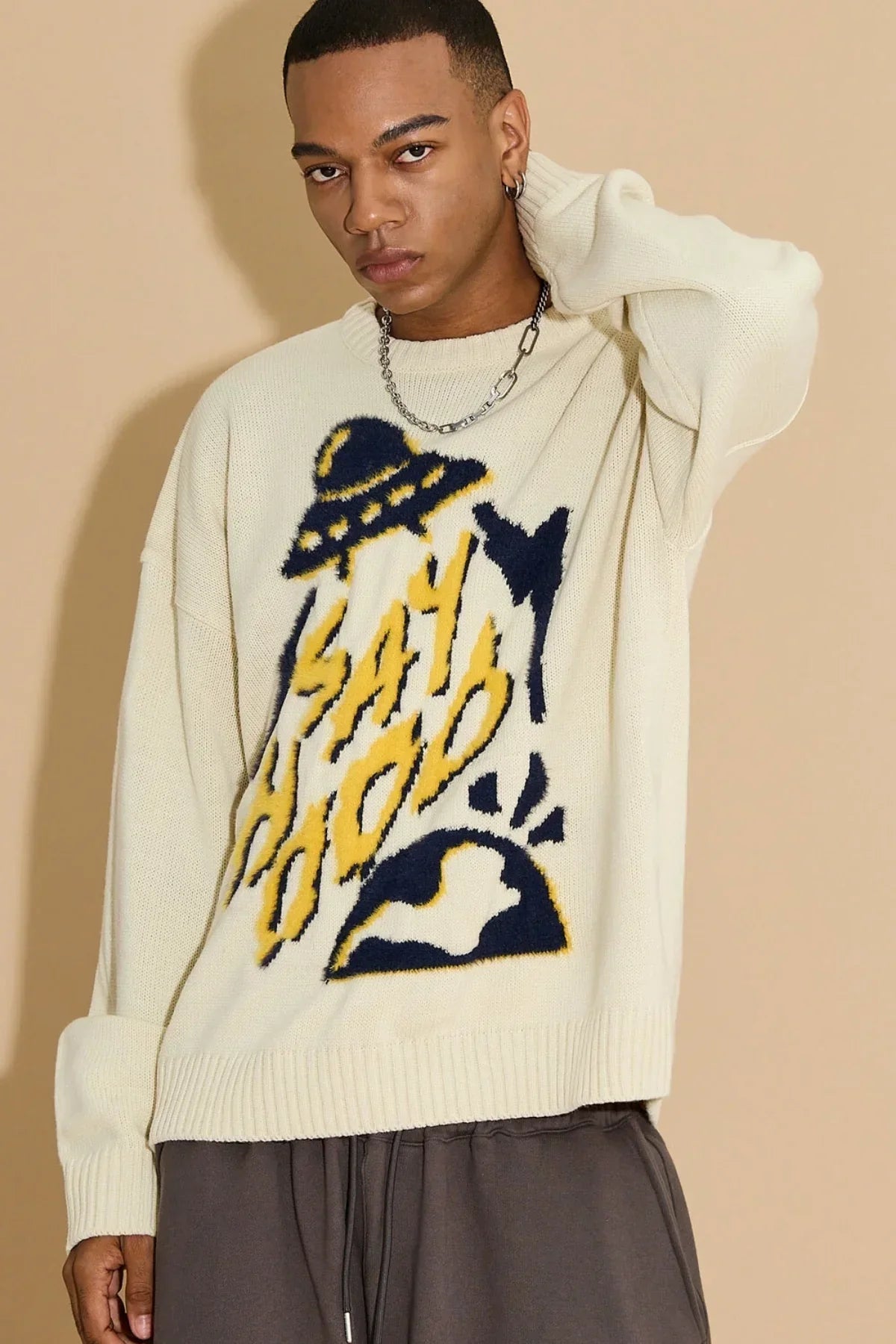 Model wearing ivory knit sweater with yellow and black 'Say Hood' graphic and dark pants