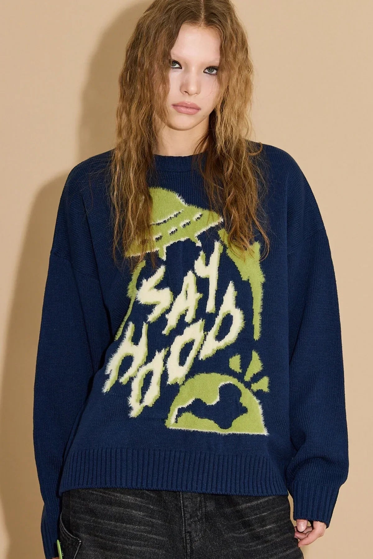 Woman wearing navy knit sweater with green and white UFO and 'Say Hood' graphic design