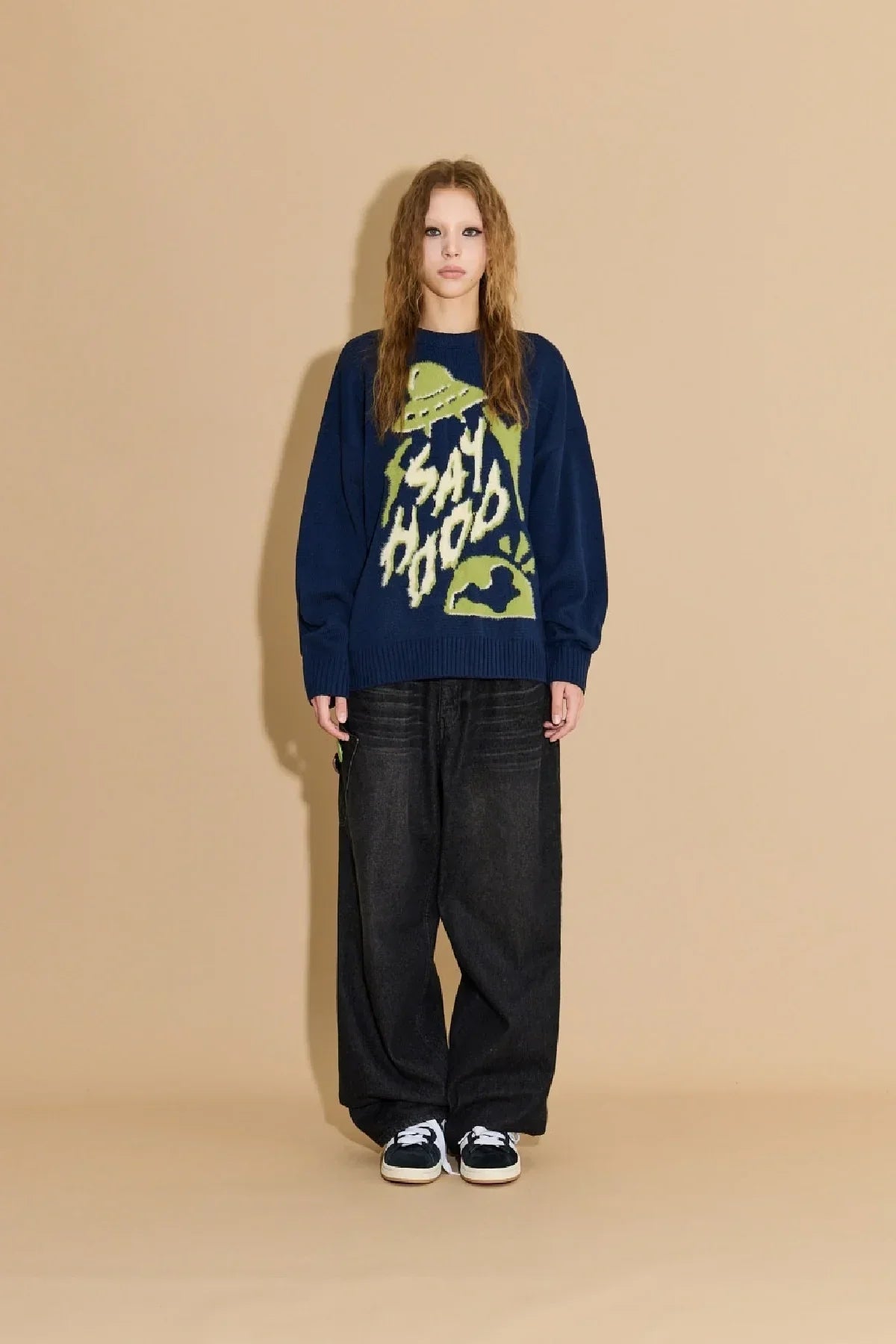 Model wearing navy blue knit sweater with green UFO and SAH HOOD text, paired with wide black pants and sneakers