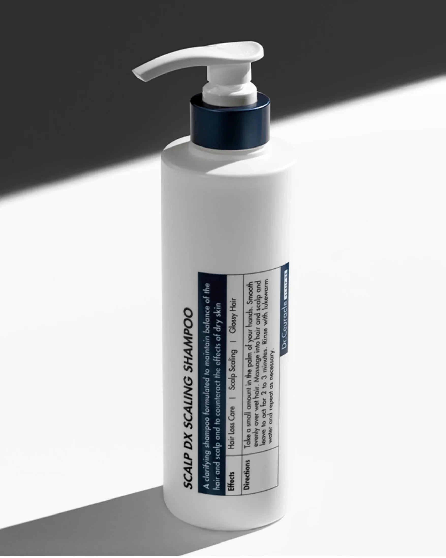 White bottle of Scalp DX Scaling Shampoo with pump dispenser on white and dark background
