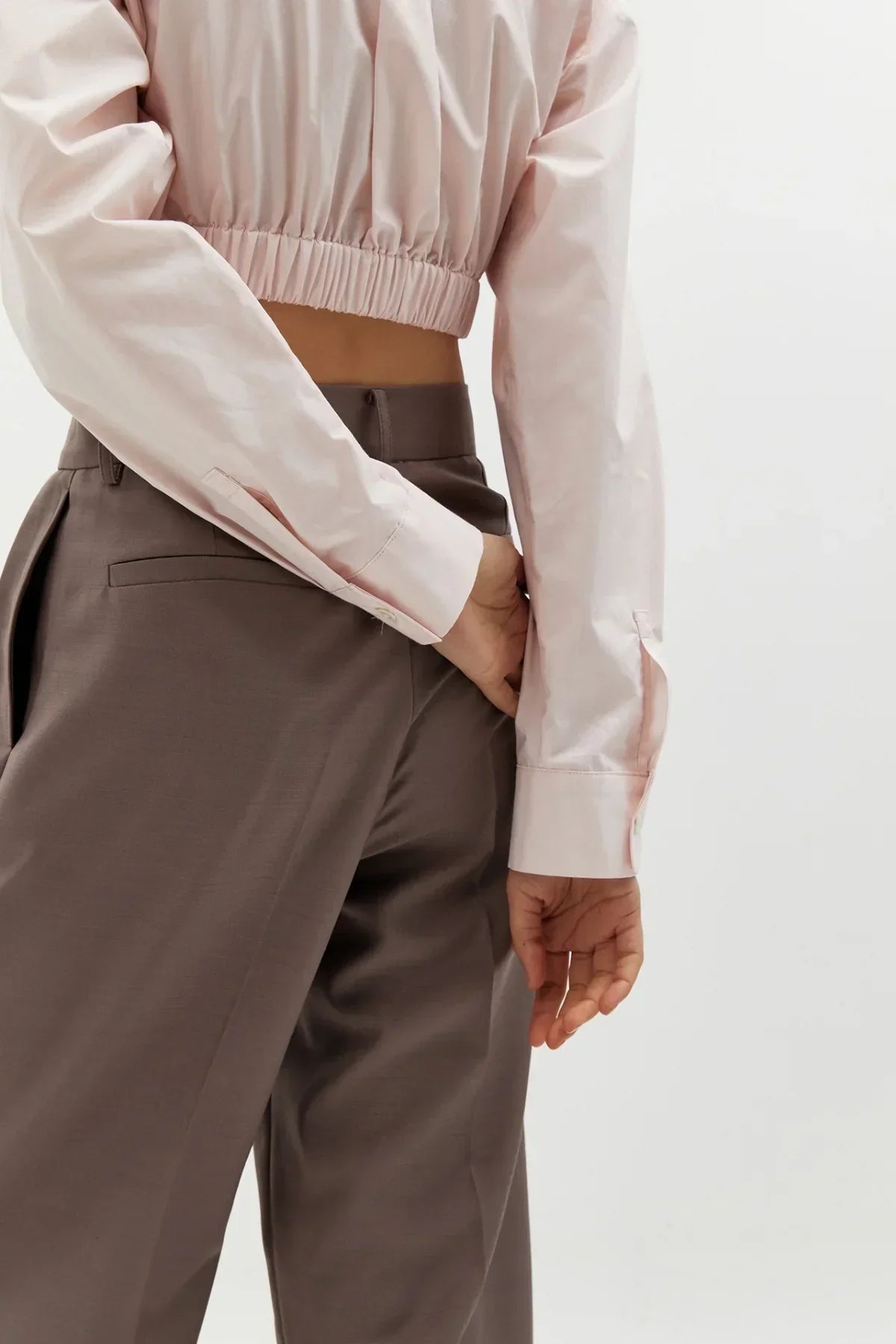 Close-up of a person wearing a pink cropped long-sleeve shirt with cuff buttons and brown high-waisted pants