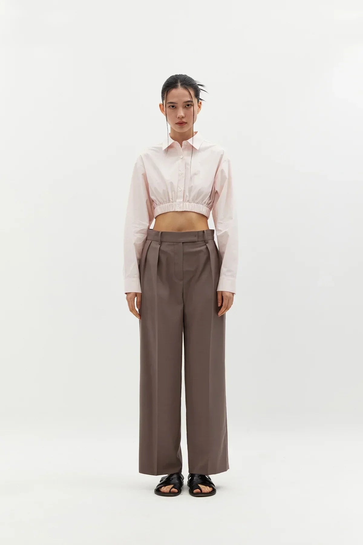 Model wearing pink cropped cotton shirt with long sleeves and brown wide-leg trousers on white background
