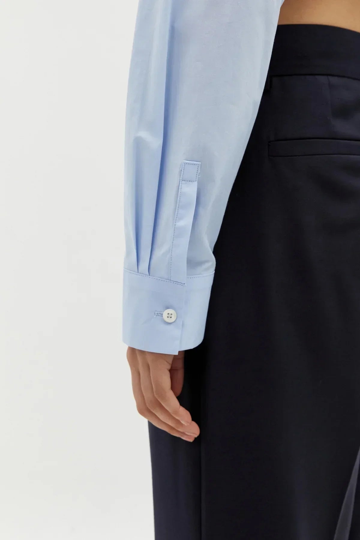 Close-up of a light blue cotton shirt cuff with button detail paired with black trousers