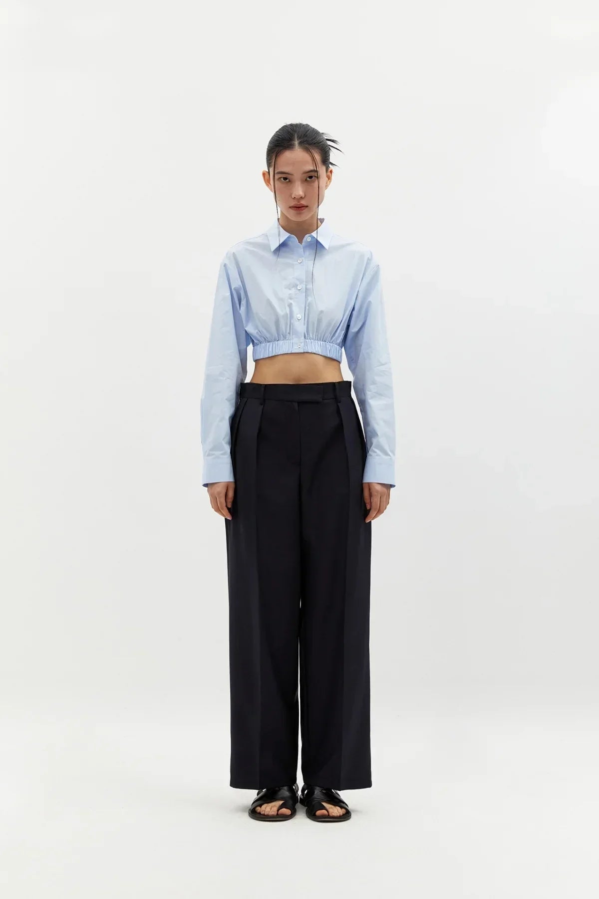 Model wearing sky blue cropped cotton shirt with long sleeves, black wide-leg pants, and black sandals