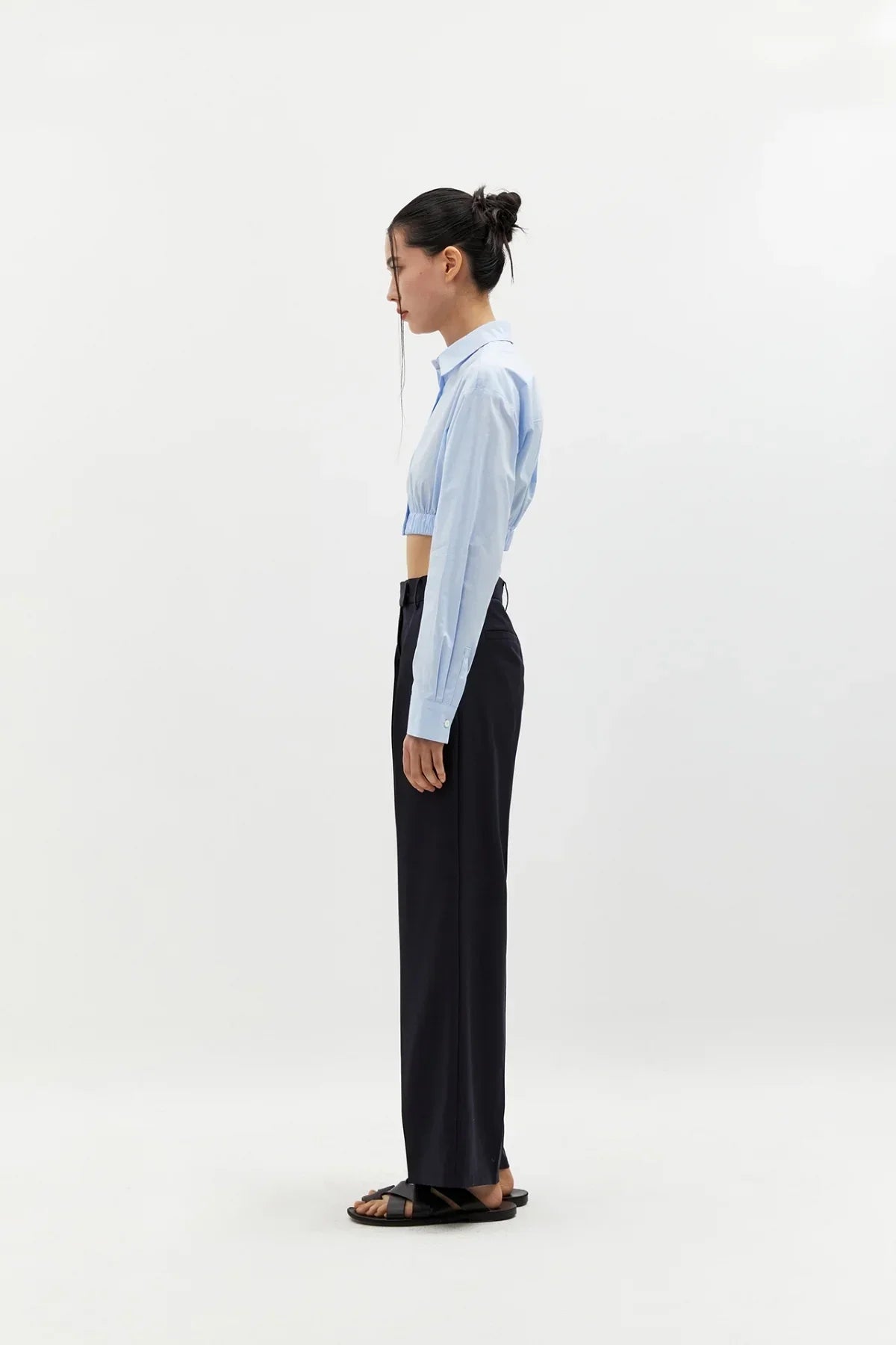 Side view of woman wearing sky blue cropped cotton shirt with long sleeves and black wide-leg pants