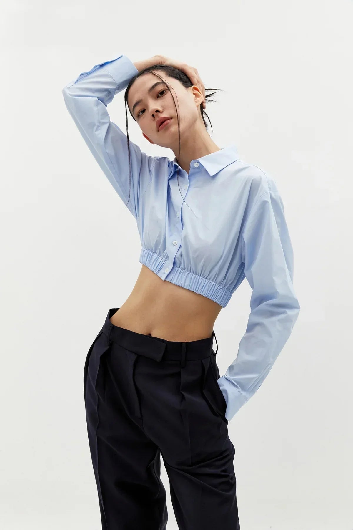 Model wearing a cropped sky blue cotton shirt with long sleeves and black high-waisted trousers