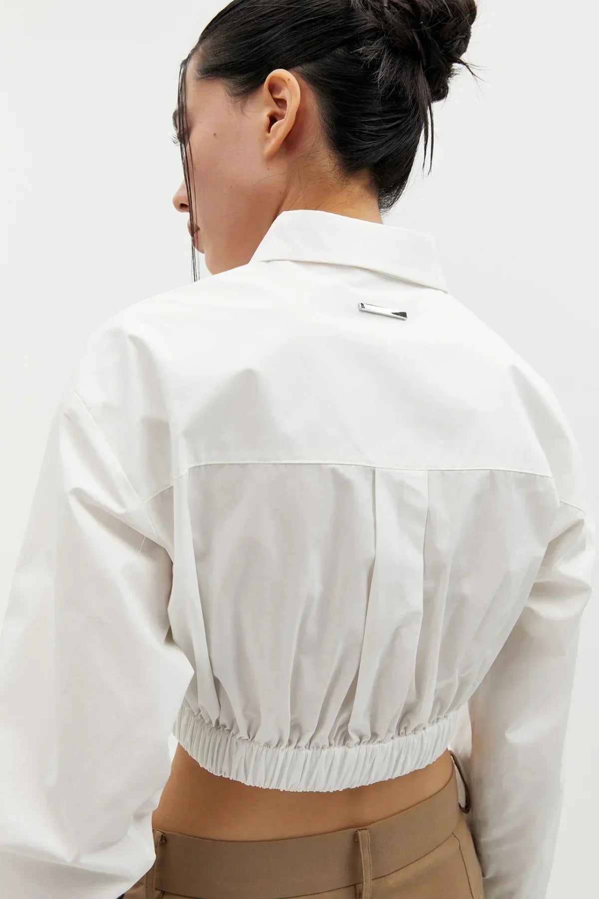 Close-up of a woman wearing a white cropped cotton shirt with elastic waistband and brown pants