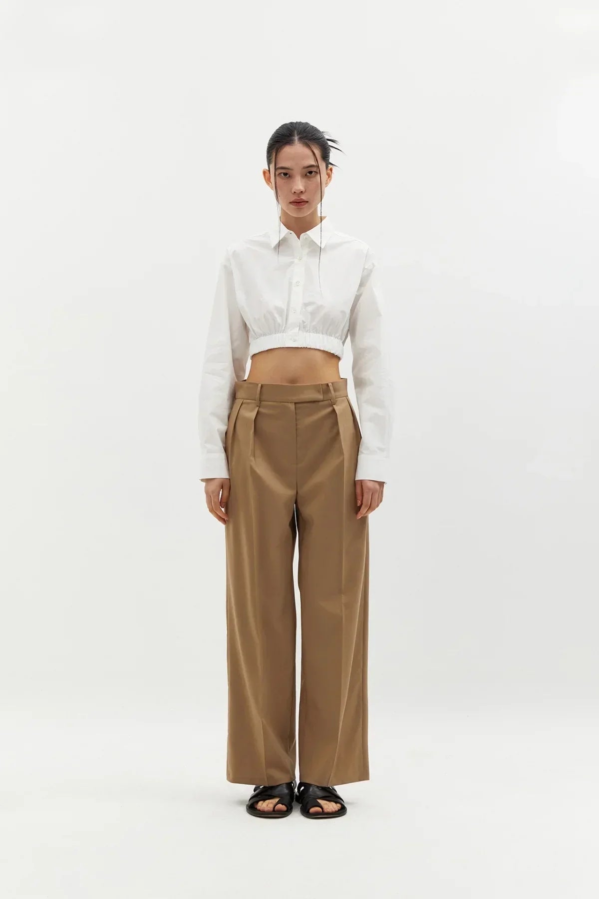 Model wearing white cropped cotton shirt and high-waisted wide-leg tan trousers with black sandals