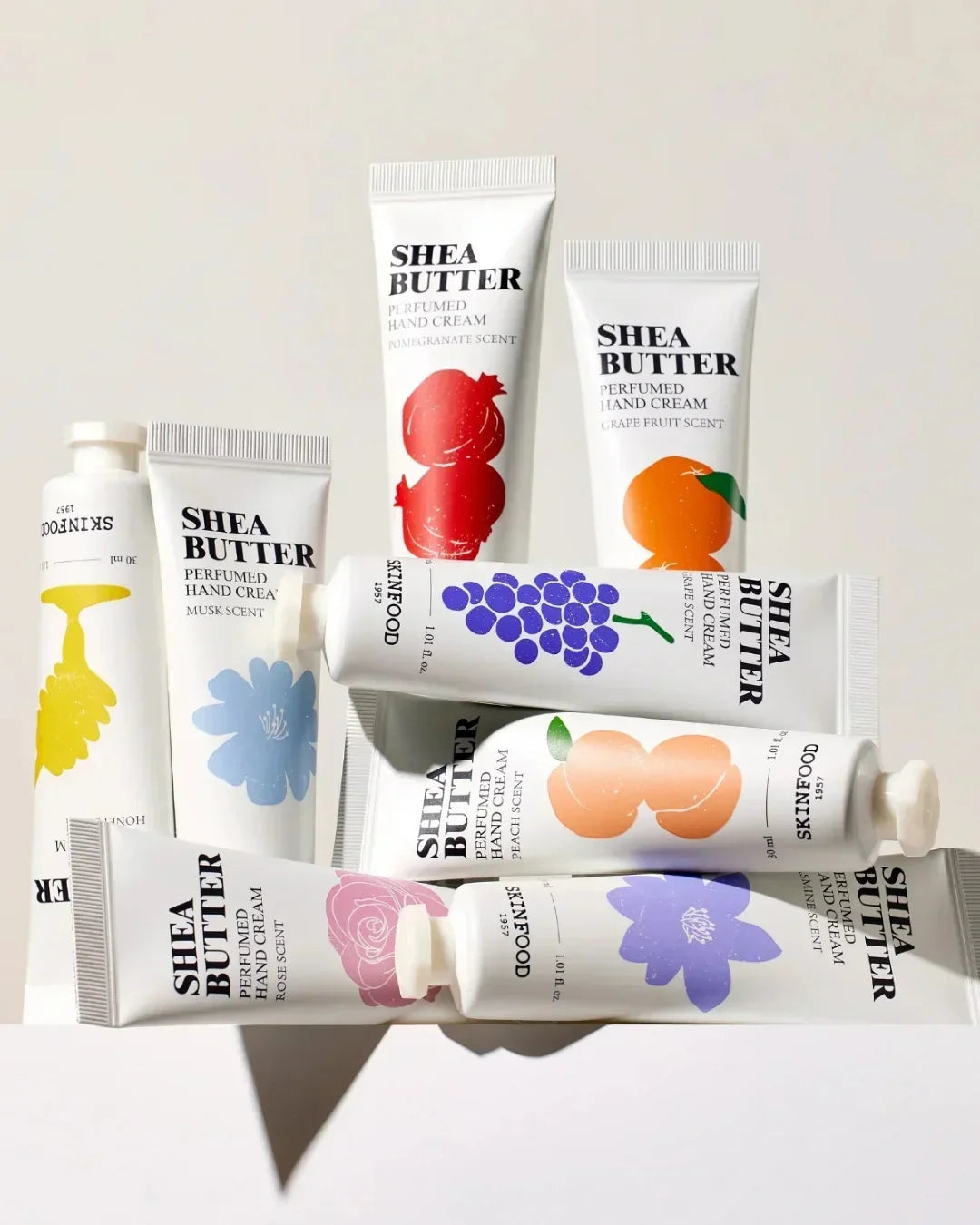 Assortment of colorful Shea Butter perfumed hand cream tubes with various fruit and floral scents on a white background